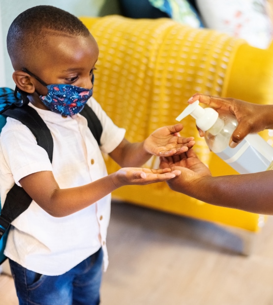 Mask-wearing young child using hand sanitizer